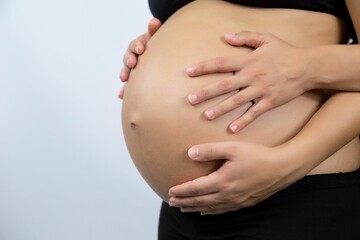 Closeup of the belly of a pregnant woman with hands holding it