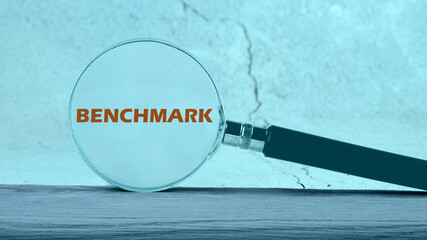 Business concept of benchmark. A word BENCHMARK written through a magnifying glass on an abstract background