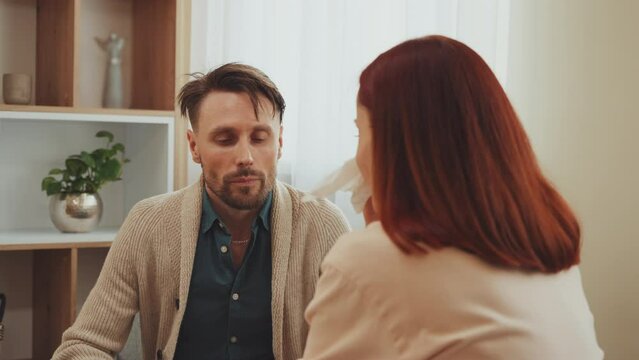 Couple in home setting during heated discussion. Man listens intently as woman expresses dissatisfaction, complaints and grievances. Female cries during intense domestic argument in living room