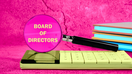 Business concept. Words BOARD OF DIRECTORS through a magnifying glass on a calculator on a bright background