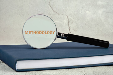 Business, study or activity concept. The word methodology written through a magnifying glass standing on a business book on a gray background