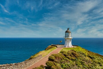 Majestic lighthouse stands at the top of a lush green hill in New Zealand, Cape Reinga