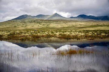 Scenic view of a lake surrounded by majestic mountain peaks on a cloudy, overcast day in Norway