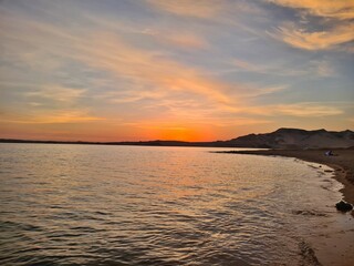 Naklejka premium Orange and pink sunrise peeking over the horizon of a tranquil beach, reflecting on the calm water