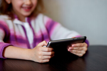 A cheerful young girl focuses on a tablet while sitting at a table, Indoors