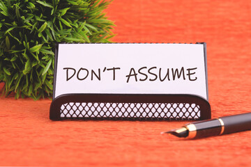 Don't assume text concept on a white business card supplied with a fountain pen and plants in...