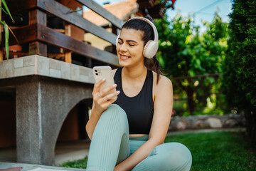 One young caucasian woman is sitting on yoga mat with wireless headphones and mobile phone preparing for training	
