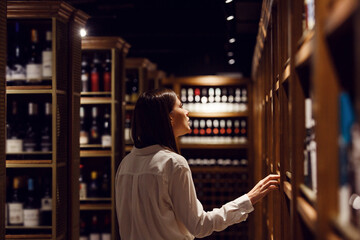 Caucasian female waiter takes wine from shelf in cellar. Sommelier choose alcohol drink for...