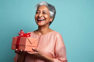 Portrait of a tender indian woman in her 60s holding a gift isolated on solid pastel color wall