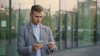 Young man in suit using information from visit card and smartphone. Slow motion