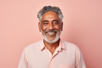 Portrait of a glad indian man in his 60s smiling at the camera in solid pastel color wall
