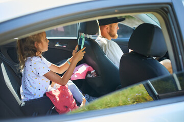 Joyful man driving car with daughter, going on trip during summer vacation