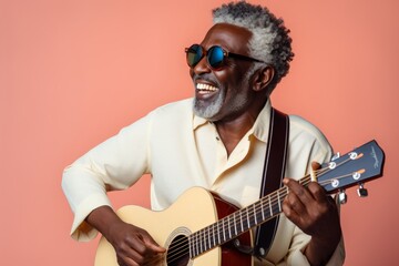 Portrait of a satisfied afro-american man in his 60s playing the guitar in front of solid pastel...