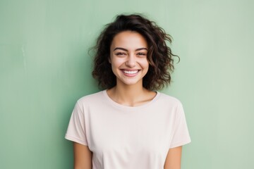 Fototapeta premium Portrait of a grinning woman in her 20s smiling at the camera in front of solid pastel color wall