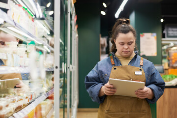 Waist up portrait of young woman with disability working in supermarket and using digital tablet for stock review copy space 