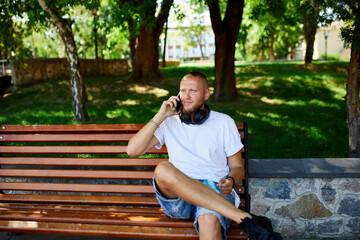 Smiling Man With Headphones Talking on Phone in Sunny Park