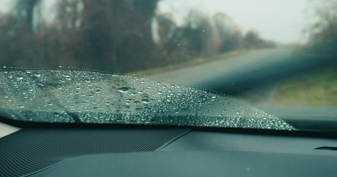Closeup shot of windscreen wiper cleaning windshield of car in light rain while parked on the road