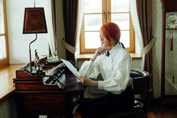 Red haired woman wearing a white blouse is sitting at a wooden desk, intently reading a letter, in...