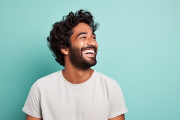Portrait of a grinning indian man in his 20s laughing while standing against solid pastel color wall