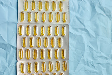 Omega 3 fish oil capsules in blister packs, showcased against a crinkled blue backdrop.