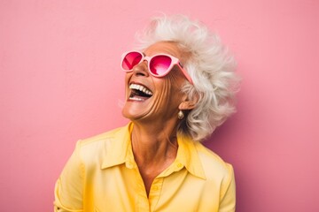 Portrait of a content woman in her 80s laughing in front of solid pastel color wall