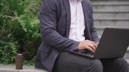 Businessman typing on the laptop while working outdoors. Close up. Slow motion