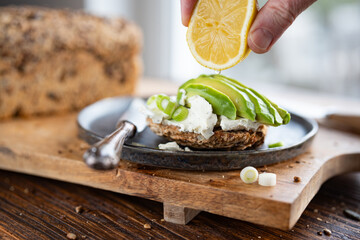 Fresh avocado slices on grain bread with cream cheese. Hand from above with lemon. Vegetarian food...