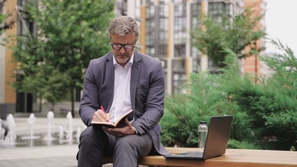 Adult man writing notes and working on the laptop outdoors. Slow motion