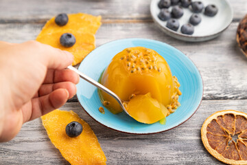Mango and passion fruit jelly with blueberry with hand on gray wooden, side view, selective focus.