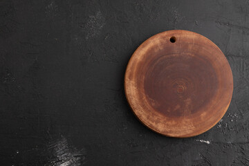 Empty round wooden cutting board on black concrete. Top view, copy space