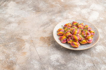 Rainbow colored dumplings with microgreen on brown concrete. Side view, copy space.