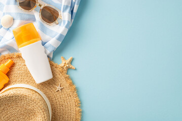Flat lay of summer vacation accessories, featuring sunscreen, sunglasses, and a straw hat on a blue...
