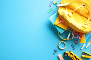 Back to School Flat Lay. A yellow backpack spills vibrant school supplies on a blue backdrop. Ideal...