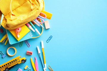 Colorful flat lay of school supplies, including a yellow backpack and a mini school bus, on a vibrant blue background. Ideal for back-to-school themes.