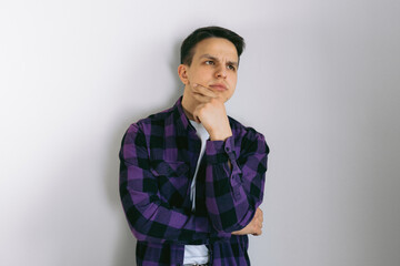 Pensive male customer looking away at copy space, touching chin, thinking. Handsome young man in casual shirt and glasses standing isolated over light background. Advertising concept