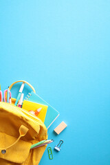 Back to school concept. Yellow backpack with colorful school supplies on vibrant blue background.