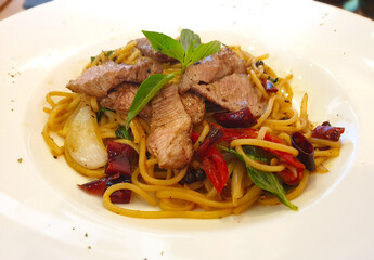 A flavorful dish of spicy beef spaghetti, garnished with fresh basil and colorful vegetables, served on a white plate
