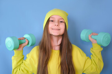 Fitness child. Portrait of sports girl with dumbbells on blue studio background. Child athlete....