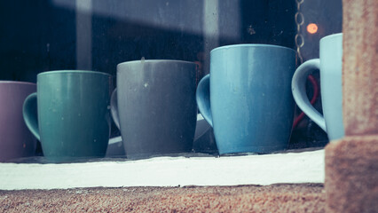 Row of coffee mugs on the cafe shelf behind the window looking in from the outside