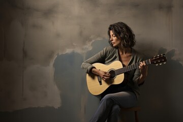 Portrait of a tender woman in her 40s playing the guitar in front of bare concrete or plaster wall