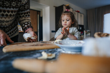 Grandmother granddaughter child kneading dough on kitchen table together. Household teamwork...