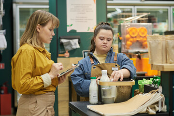 Portrait of young woman with Down syndrome training in supermarket and helping customers with...