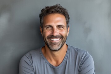 Obraz premium Portrait of a grinning man in his 40s smiling at the camera on bare concrete or plaster wall