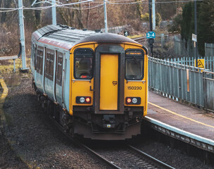 Obraz premium yellow and silver train pulling into a station area with a bridge in the background