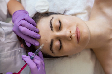 Cosmetologist making rejuvenating anti wrinkle injections on the face of a beautiful woman. Female...