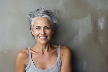 Portrait of a blissful woman in her 50s smiling at the camera in front of bare concrete or plaster wall
