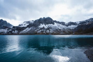 Scenic blue lake enveloped by majestic mountain peaks under cloudy skies