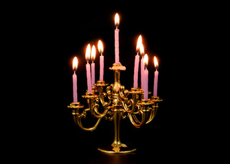 Gold candelabra with many purple burning candles isolated on black background.	