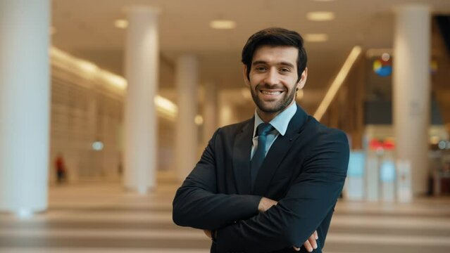Professional business man turn around while standing with arm folded. Happy caucasian investor looking at camera with confident while crossing arm at hall with blurring background. Portrait. Exultant.