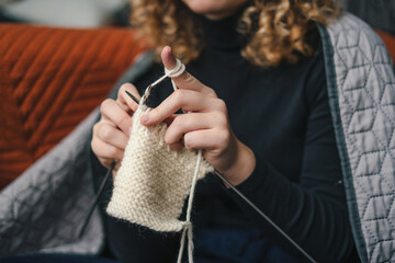 Hands of an unrecognizable young woman knitting product from white woolen thread. Young woman...
